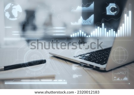 Close up of laptop on wooden desk with pen and business charts hologram on blurry background. Military control, world economy and finances virtual diagram. Double exposure