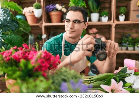 Young hispanic man florist holding professional camera at flower shop