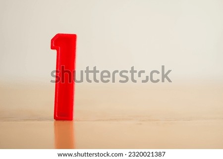Red plastic number 1 (one) sign stand on wooden table white background with copy space. Successful, leadership, top, triumph and winner concept.