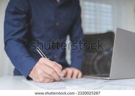 Businessman hand holds pen for writing on business paperwork for accept agreement contract on business investment or project. Young adult business man signing on financial document deal. Copy space