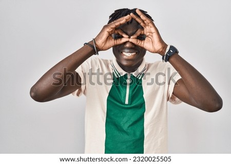 African man with dreadlocks standing over isolated background doing ok gesture like binoculars sticking tongue out, eyes looking through fingers. crazy expression. 