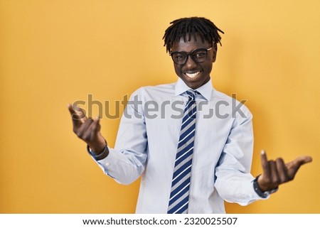 African man with dreadlocks standing over yellow background shouting with crazy expression doing rock symbol with hands up. music star. heavy concept. 