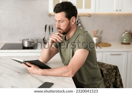 Soldier with notebook at white marble table in kitchen. Military service
