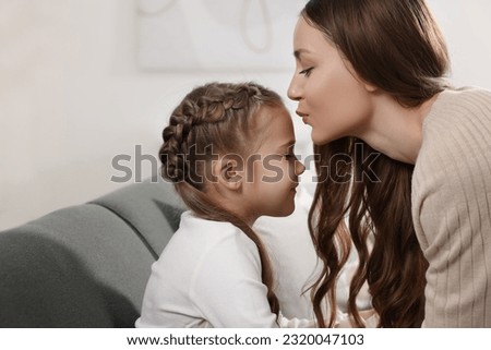 Happy mother kissing her cute daughter on sofa at home