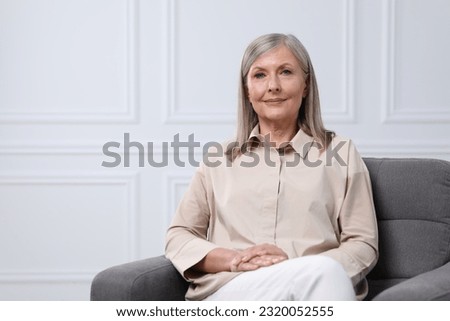 Portrait of beautiful senior woman in armchair indoors. Space for text
