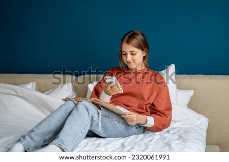 Teen girl reading book photographing page on smartphone to share in social media sitting in bed at home. Caucasian teenager bookworm nerd kinds of literature. Leisure, taking picture on mobile phone. Royalty-Free Stock Photo #2320061991