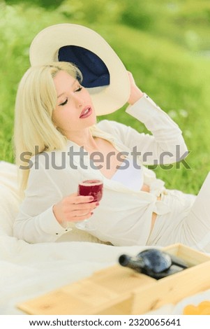 A woman with a hat in her hand and a glass of wine. Blond woman lying on a bedspread at rest. Picnic.