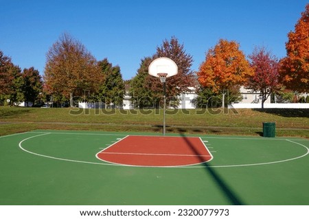 An outdoor basketball court seen in the fall season with a beautiful trees in the background with colorful leaves