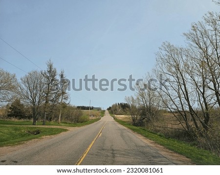 An open rural road with farm land on either side of it.