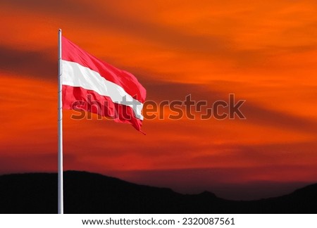 Waving Austrian flag against a red sky with clouds at sunset and empty space for text. Room for text.