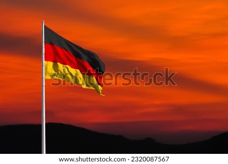Waving German flag against a red sky with clouds at sunset and empty space for text. Room for text.