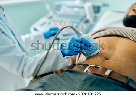 Close up of doctor using ultrasound while examining abdomen of African American male patient.  Royalty-Free Stock Photo #2320101225