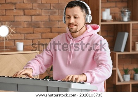 Male musician with headphones playing synthesizer at home Royalty-Free Stock Photo #2320103733