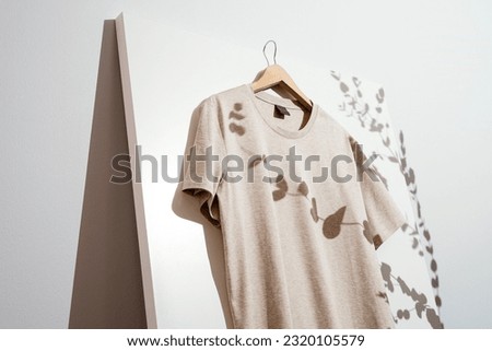 Blank beige t-shirt mockup, template on wooden hanger with eucalyptus leaves shadow over white background