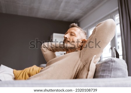 Older Man Leaning Relaxingly on His Sofa with Closed Eyes, Gazing Upwards Royalty-Free Stock Photo #2320108739