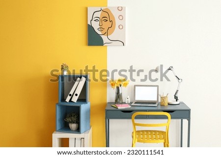 Stylish workplace with modern laptop, beautiful narcissus flowers and picture on wall