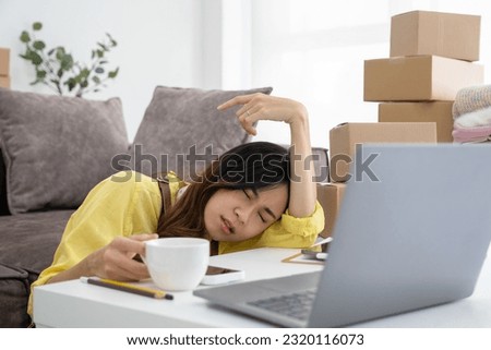 Young businesswoman or online business owner as she finds herself amidst cardboard boxes, seated at her desk battling fatigue and confusion, determined to find solutions for her work. 