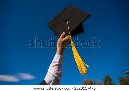 Close-up of a woman's hand with a graduation cap against the blue sky.  Royalty-Free Stock Photo #2320117475