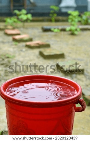 Vibrant essence as raindrops elegantly descend into a red bucket, creating mesmerizing ripples in the water, a symphony of nature's artistry