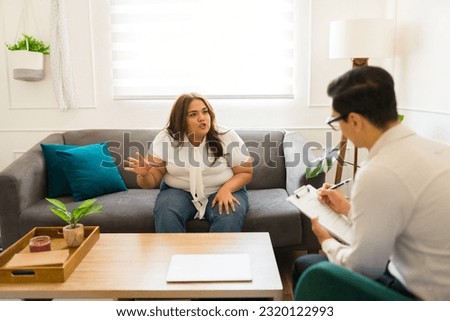 Upset hispanic woman with anger issues talking and screaming to her therapist while coming to anger management Royalty-Free Stock Photo #2320122993