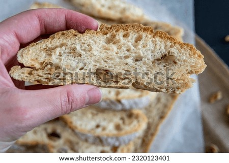 Hand holding a slice of homemade walnut bread, traditional sourdough bread loaf cut into slices on a rustic board and baking paper. Sliced bread with golden bread crust. Healthy eating concept.