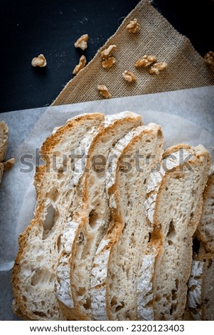 Slices of homemade walnut bread, traditional sourdough bread loaf cut into slices on a dark rustic board and baking paper. Sliced bread with golden bread crust. Healthy baking concept.