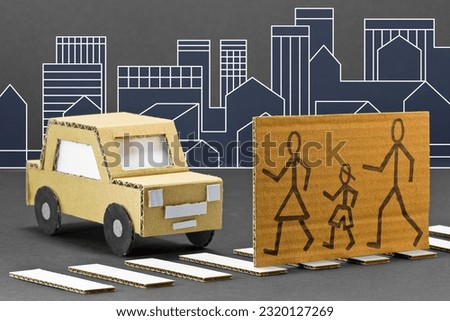 Black and white pedestrian crossing with cardboard stopped car and pedestrians cross the road safely - cartoon concept against a cityscape