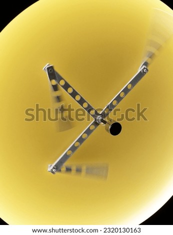 scientific experiment on kinetic energy with pieces of metal attached to the ends of a central 3-sided piece that rotates the other three pieces rapidly inside a yellow circle.
