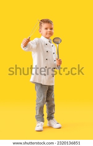 Cute little chef with supplies on yellow background Royalty-Free Stock Photo #2320136851