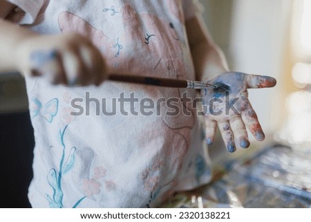 Close up of little girl painting on her own hand with tempera paint,.