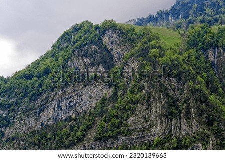 Scenic landscape with cliff and woodland at lakeshore of Lake Lucerne seen from passenger ship on Lake Lucerne on a cloudy spring day. Photo taken May 18th, 2023, Treib, Canton Uri, Switzerland.