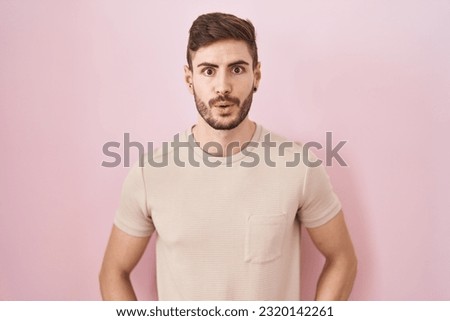 Hispanic man with beard standing over pink background afraid and shocked with surprise and amazed expression, fear and excited face. 