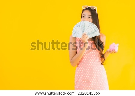Portrait beautiful young asian woman with a lot of cash and money with piggy bank on yellow isolated background