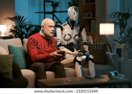 Senior man and female humanoid robot sitting on the couch at home and playing video games together