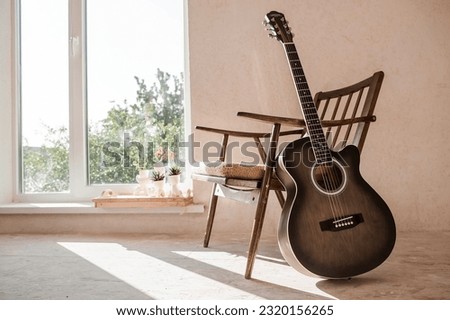 Guitar. Guitar chords. Acoustic guitar. Music. Musical background. An image of an acoustic guitar in a room with a retro armchair. Hard light. Shadows. Royalty-Free Stock Photo #2320156265