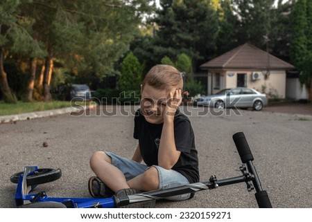 Kid hurts his forehead after falling off his scooter. Child is learning to ride a scooter. the boy hit his head on the asphalt Royalty-Free Stock Photo #2320159271