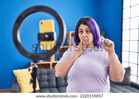 Plus size woman wit purple hair recording bitcoin tutorial with smartphone at home covering mouth with hand, shocked and afraid for mistake. surprised expression 