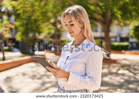 Young blonde woman smiling confident using touchpad at park