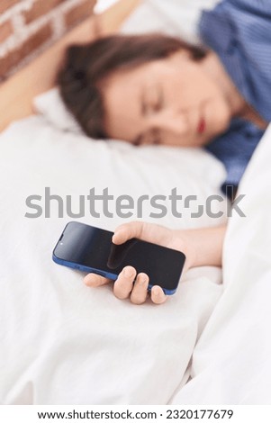 Middle age woman holding smartphone sleeping at bedroom