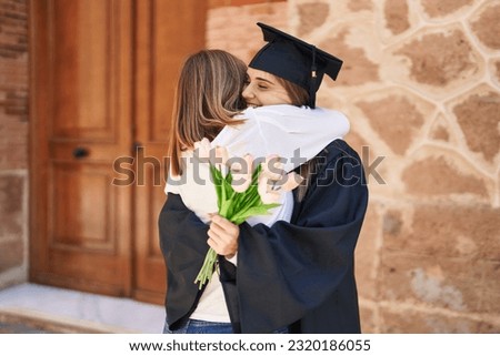 Two women mother and graduated daughter holding flowers at campus university Royalty-Free Stock Photo #2320186055