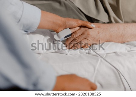 Closeup to the camera family member lady giving support to his grandfather or dad while he is on the hospital room laying on the bed and waiting for a health checkup Royalty-Free Stock Photo #2320188525