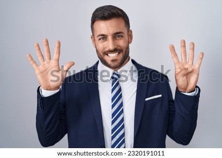 Handsome hispanic man wearing suit and tie showing and pointing up with fingers number nine while smiling confident and happy.  Royalty-Free Stock Photo #2320191011