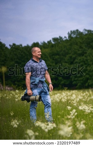 Professional nature photographer in the field by the forest, holding camera with a long telephoto lens