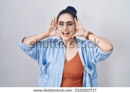 Young modern girl with blue hair standing over white background smiling cheerful playing peek a boo with hands showing face. surprised and exited 