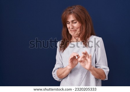Middle age woman standing over blue background disgusted expression, displeased and fearful doing disgust face because aversion reaction. with hands raised 