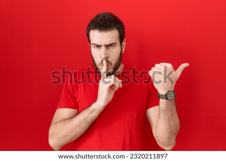 Young hispanic man wearing casual red t shirt asking to be quiet with finger on lips pointing with hand to the side. silence and secret concept. 