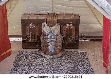 scene in horizontal view of an old trunk and ancient roman soldier armor cuirass "Lorica Musculata" inside a soldier military tent from ancient rome Royalty-Free Stock Photo #2320215631