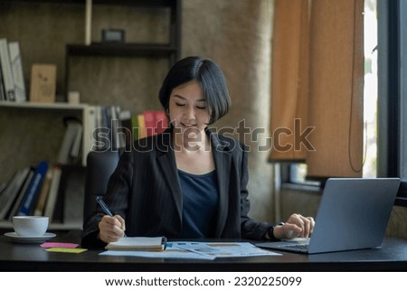 Happy young asian businessman sitting on her desk in the office Young woman working on laptop. Search and take a note.