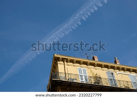 Contrails after a jet plane are visible in the blue sky next to an old nice house with apartments.