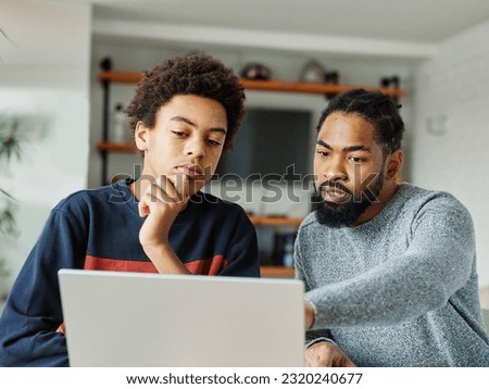 Father and son doing homework with laptop at home. Father and teenage son using laptop. Boy and dad sitting at home working with notebook Royalty-Free Stock Photo #2320240677